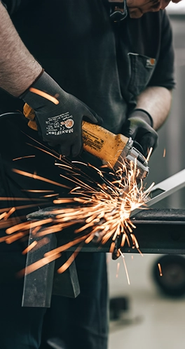 A welder cuts a piece of steal with a grinder. Sparks fly out.